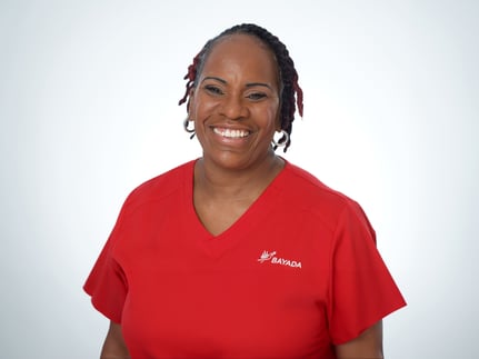 Karen Dixon stands smiling in front of a white background, wearing a red BAYADA branded scrub top