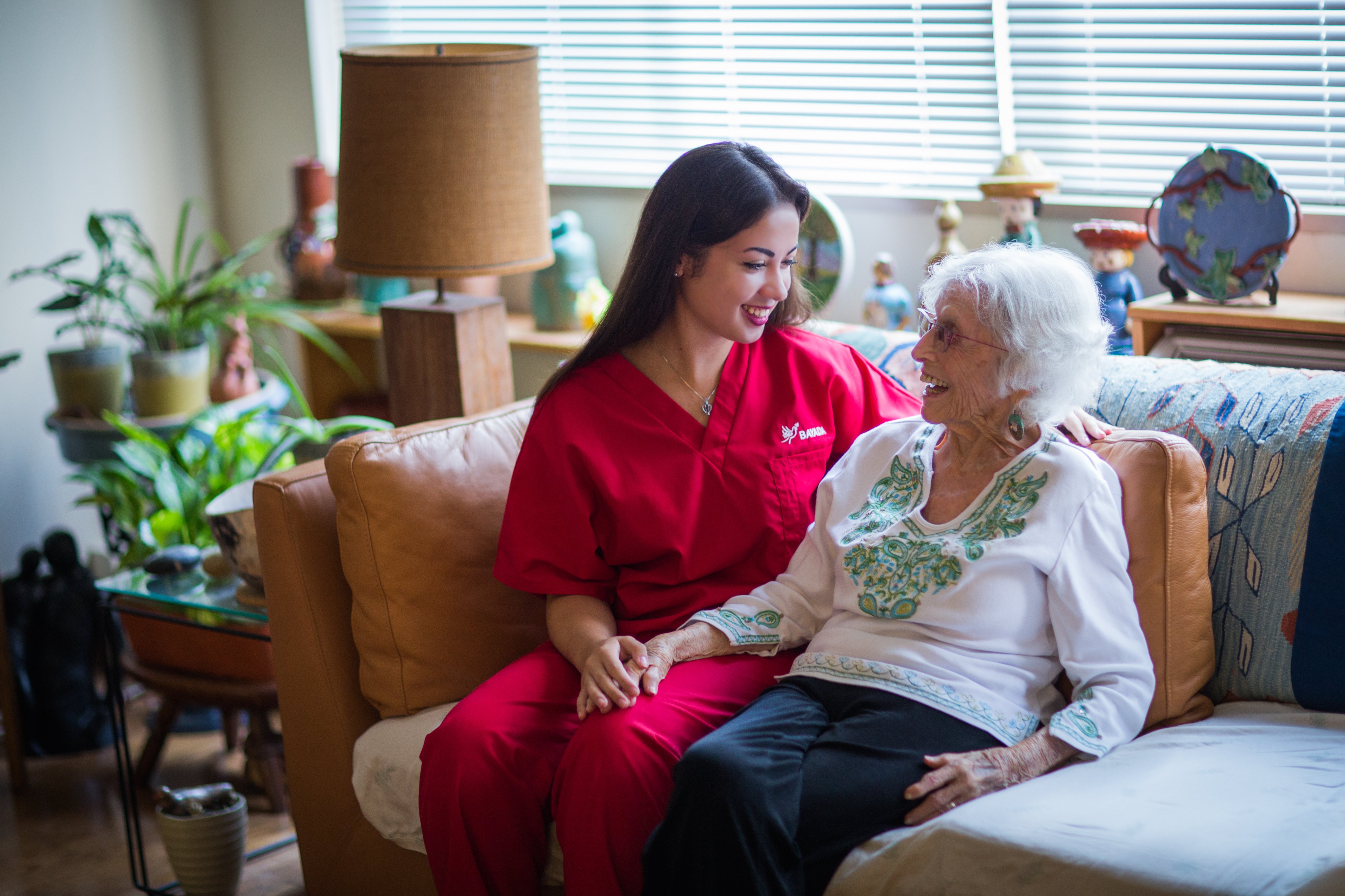 Home health aide sits on couch with her client.