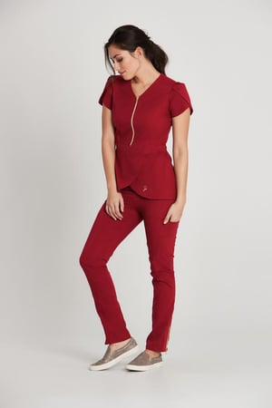 A woman standing up in dark red scrubs. She is looking down.